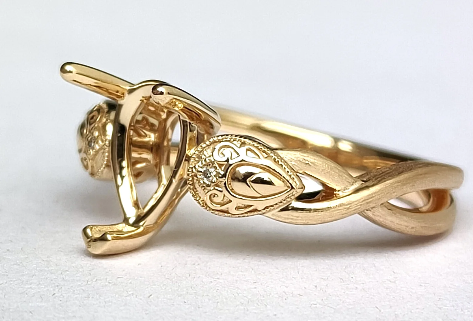 The same ring from the side, with satin strands crossing along the band beside a polished carved shoulder.