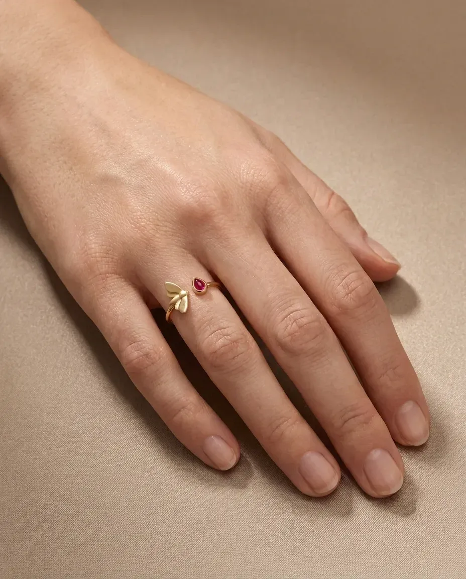 Design visualisation of the Sholeh Ring worn on the hand: an open gold ring with a small moth on one end and a ruby teardrop on the other.