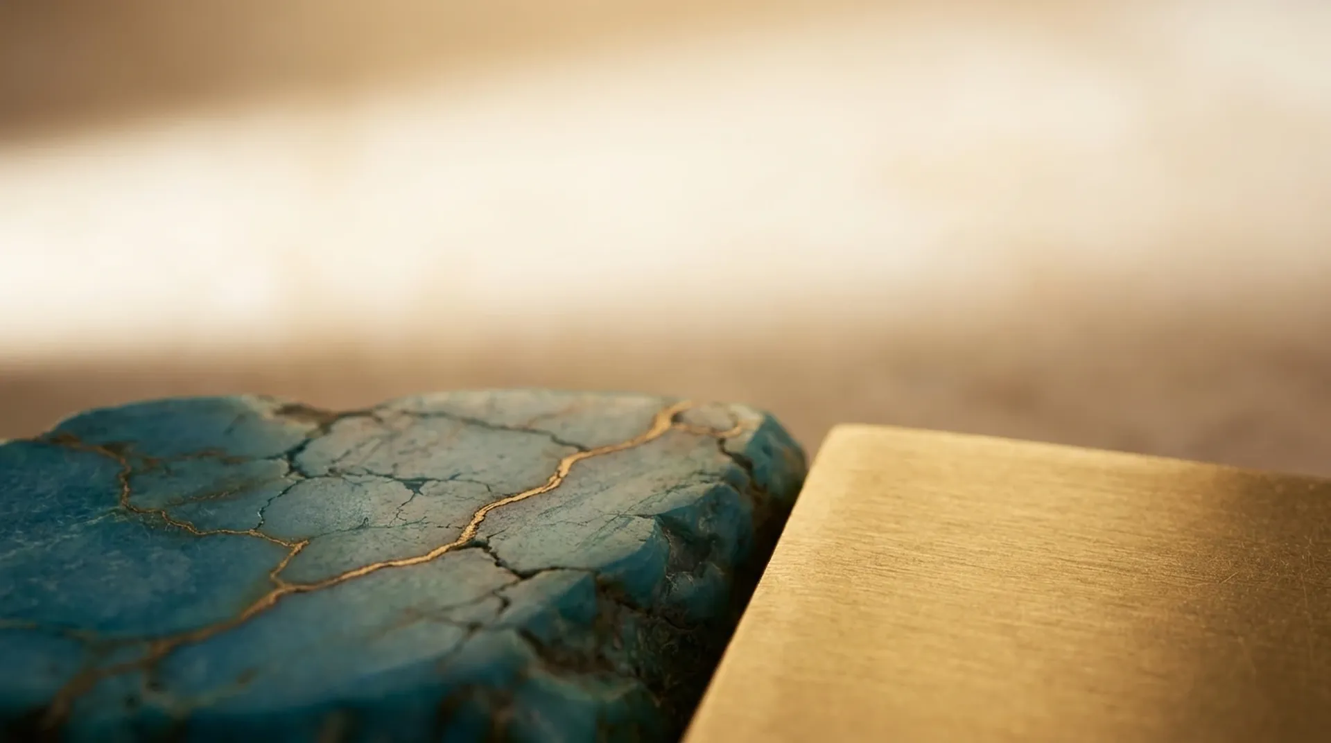 A raw turquoise stone with golden matrix veining resting beside the brushed edge of a gold sheet