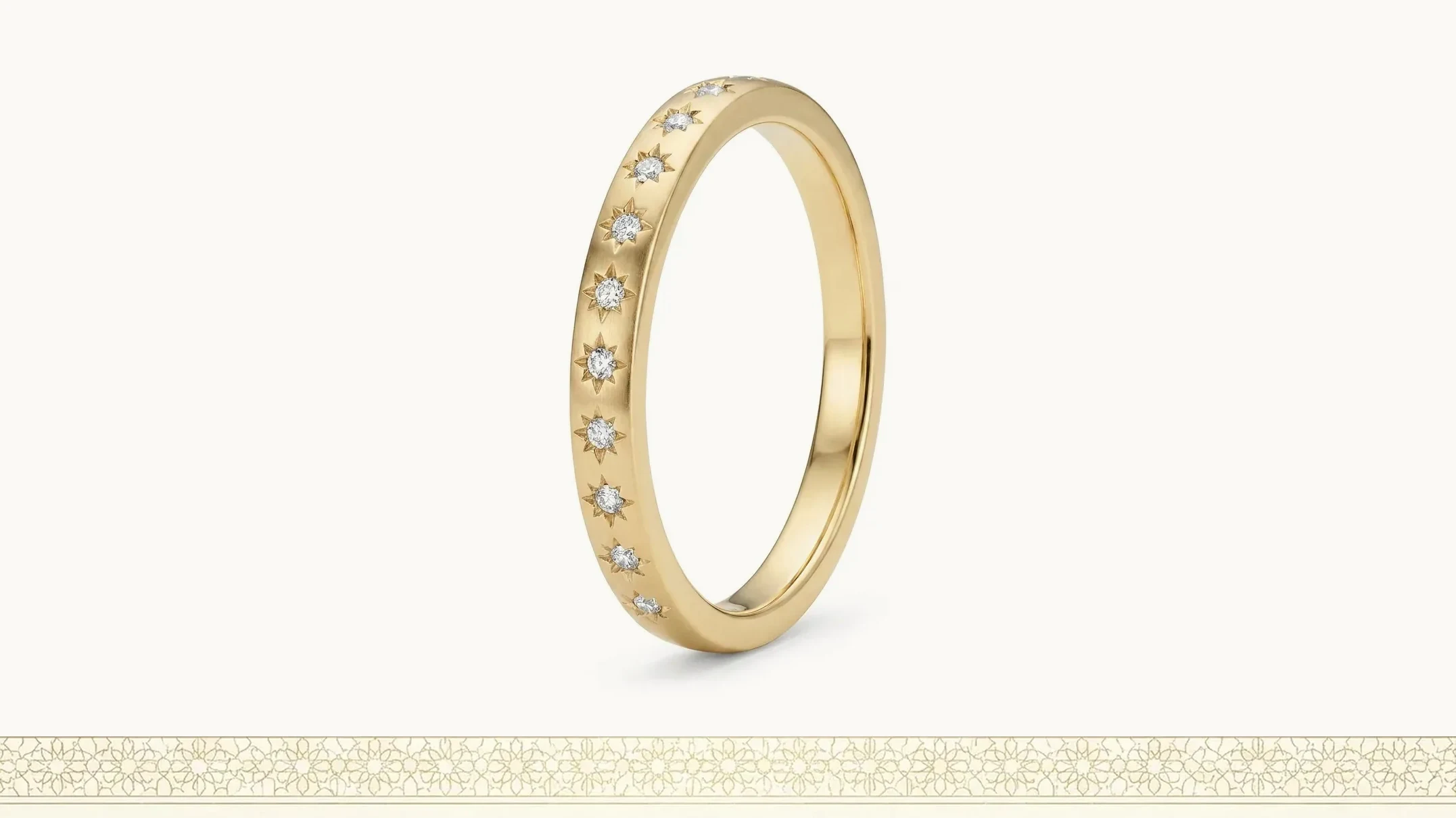 A slim gold band set with small star-set diamonds, photographed on a plain ground